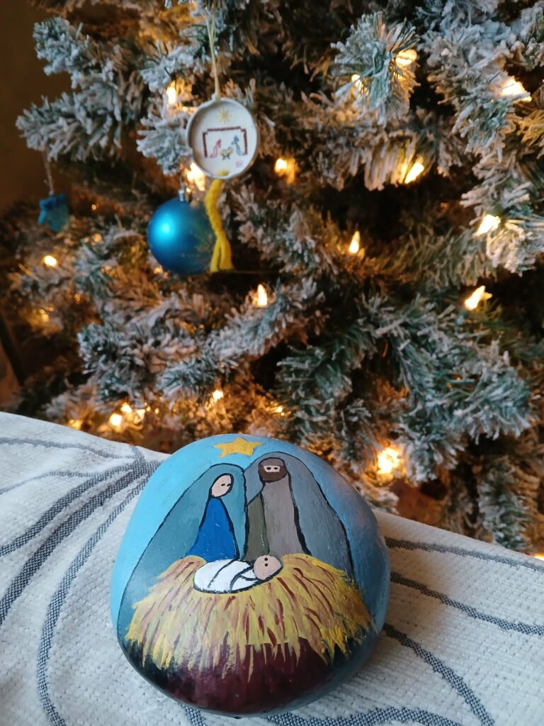 Manger scene painted on a rock in front of the Christmas tree